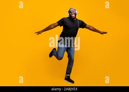 Ich glaube fliegen kann. Volle Größe phtoo Lustige positive afro-amerikanische Kerl hören Musik mit Headset singen song Hände heben wie Vögel Flügel tragen t-shirt Stockfoto