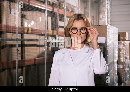 Zuversichtlich Lagerhalter im weißen Mantel berühren Brille und Kamera suchen Stockfoto