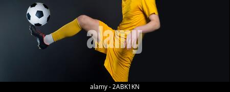 Nahaufnahme Beine und Fußball Schuh des Fußball-Spieler in Aktion treten Ball auf schwarzem Hintergrund tragen gelbe Jersey und Socke isoliert Stockfoto