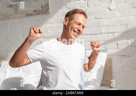 Lächelnde Menschen ausdehnen, während auf dem Bett am Morgen sitzen Stockfoto