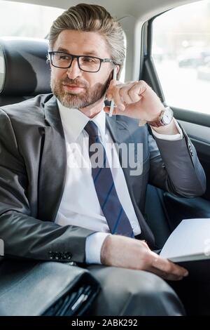 Selektiver Fokus der stattlichen Diplomat sprechen auf Smartphones im Auto. Stockfoto