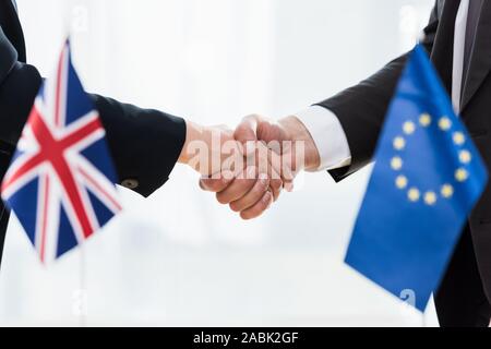 7/8-Ansicht von Diplomaten Händeschütteln in der Nähe von Europäische Union und Großbritannien Flaggen Stockfoto