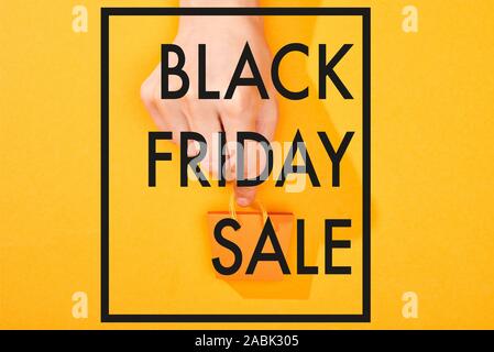 7/8-Ansicht von Hand kleine Einkaufstasche auf orangefarbenem Hintergrund mit schwarzem Freitag verkauf Abbildung: Stockfoto