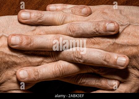 Farbe Foto des älteren Mannes Hände mit gekreuzten Fingern, auf einer hölzernen Hintergrund Stockfoto