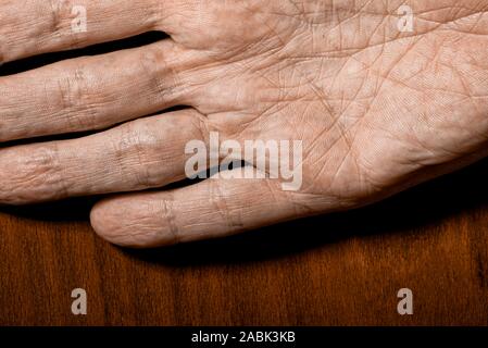 Bild der älteren männlichen Händen auf einer hölzernen Hintergrund. Detail der Handfläche. Stockfoto