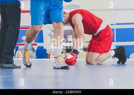 Zwei Boxer in den Boxring. Knockout und Geschmack der Niederlage. Boxer kniend mit gesenktem Kopf. Bild horizontal. Stockfoto