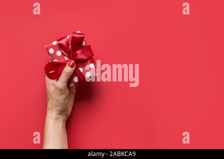 Frau Hände, die Geschenkverpackung mit roter Schleife und weißen Punkten. Grußkarte. Boxing Day. Blick von oben. Platz kopieren Stockfoto