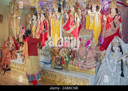 Eine ältere Hinduistische Frau übernimmt die aarti Ritual der schwenkten Flammen vor den Statuen von Gottheiten. An einem Tempel in Queens, New York City. Stockfoto