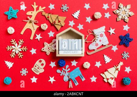 Blick von oben auf die Holz- Kalender, urlaub Spielzeug und Dekorationen auf rot Weihnachten Hintergrund. Der erste Januar. Neues Jahr Zeit Konzept. Stockfoto