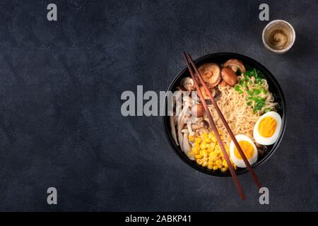 Ramen. Soba Nudeln mit Ei, Shiitake und enoki Pilze, Mais und Frühlingszwiebeln, geschossen von oben auf einem dunklen Hintergrund mit Stäbchen, Sake Stockfoto