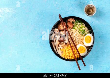 Ramen. Soba Nudeln mit Ei, Shiitake und enoki Pilze, Mais und Frühlingszwiebeln, geschossen von oben auf einem blauen Hintergrund mit Stäbchen, Sake Stockfoto