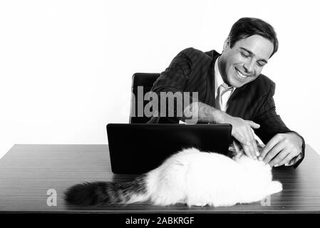 Studio shot der Jungen glücklich Persischen Geschäftsmann lächelnd und berühren süße Katze sitzend mit Laptop auf hölzernen Tisch Stockfoto