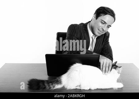 Studio shot der jungen Persischen Geschäftsmann berühren süße Katze sitzend mit Laptop auf holztisch vor weißem Hintergrund Stockfoto