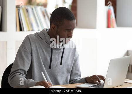 Schwere schwarze männliche Kursteilnehmer mit Laptop, beschäftigt sich mit der Untersuchung. Stockfoto