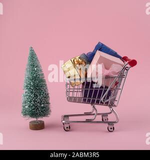 Christmas shopping Konzept, shop warenkorb Trolley mit Weihnachtsbaum und Geschenkbox auf Rosa Stockfoto