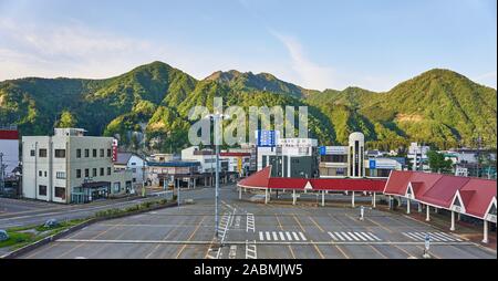 Die leeren Parkplatz, Berge, Bushaltestellen, Wartebereich, und Geschäfte außerhalb der Ausgang Ost von echigo-yuzawa Station auf einen späten Frühling Abend. Stockfoto