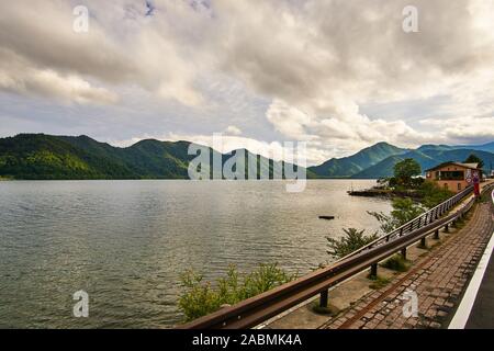 Berge drapiert in Grün und Wolken' shaddows Surround Chuzenji See (Chuzenji-ko) an einem bewölkten Sommertag, in Nikko, Tochigi, Japan Stockfoto