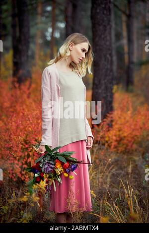 Mädchen gehen in den Wald. Einen schönen großen Blumenstrauß in den Händen einer Frau. Mädchen steht in Gelb, Rot, Gras, Herbst Natur Stockfoto