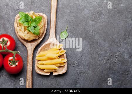 Verschiedene Pasta in Löffel und Zutaten zum Kochen. Tomaten und Basilikum. Ansicht von oben flach mit Kopie Raum Stockfoto