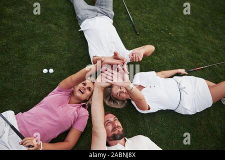 Vier Menschen, zwei Jungs und zwei Mädchen, liegen auf dem Golfplatz und entspannen Sie nach dem Spiel Stockfoto