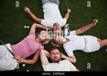 Vier Menschen, zwei Jungs und zwei Mädchen, liegen auf dem Golfplatz und entspannen Sie nach dem Spiel Stockfoto