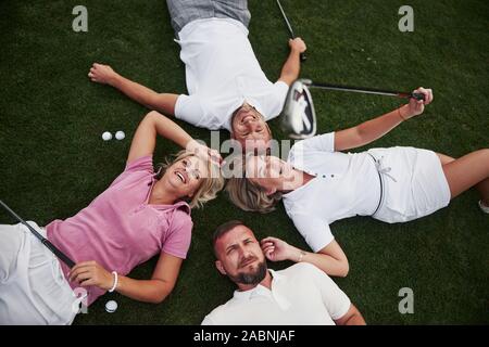 Vier Menschen, zwei Jungs und zwei Mädchen, liegen auf dem Golfplatz und entspannen Sie nach dem Spiel Stockfoto