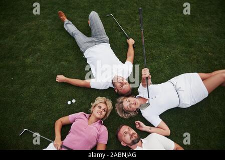 Vier Menschen, zwei Jungs und zwei Mädchen, liegen auf dem Golfplatz und entspannen Sie nach dem Spiel Stockfoto