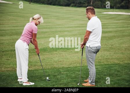 Mädchen spielen Golf und das Schlagen von Putter auf Grün. Ihr Lehrer hilft die Technik zu erkunden und Ihre erste Streiks machen Stockfoto