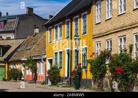Lund, Schweden - 24. Juni 2018: Kleine Hütten auf einem gepflasterten Straße im historischen Teile der Universitätsstadt Lund. Sommer und Rosen. Stockfoto