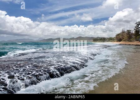 Hohe Brandung und Wellen um vulkangestein an einem Sandstrand an einem bewölkten Tag mit zartem Sonnenlicht, Kapa'a, Kauai, Hawaii Stockfoto