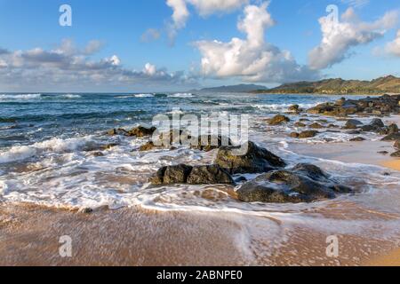 Hohe Brandung und Wellen um vulkangestein an einem Sandstrand kurz nach Sonnenaufgang an einem bewölkten Morgen mit zartem Sonnenlicht, Kapa'a, Kauai, Hawaii Stockfoto