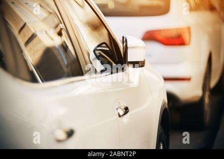 Ein weißes Auto mit einem Rückspiegel, die Fenster, die Gebäude auf einem Sommer sonnigen Tag, steht hinter einem weißen Auto. Stockfoto