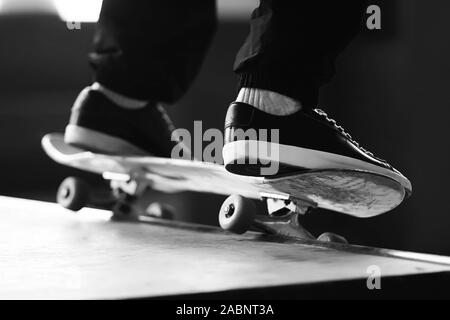 Ein schwarz-weißes Bild der Füße ist ein Mann, der elegante Mode sneakers gekleidet, eine Folie auf einem Skateboard auf der Rampe. Stockfoto