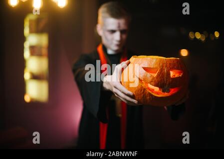 Junger Mann in Halloween Kostüm mit einem geschnitzten Kürbis auf seinen ausgestreckten Arm Stockfoto