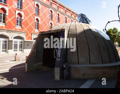 Tirana, Albanien - September 29, 2019: Nahaufnahme des gewölbten Beton Bunker Eingang zu einem Etagenbett 'Kunst 2 Museum mit der Orange und Gold plaid Fassade des Stockfoto