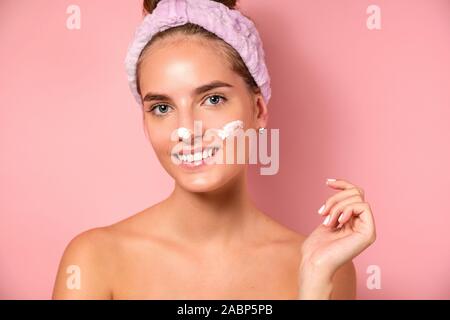 Ein Mädchen mit sauberen Haut steht auf einem rosa Hintergrund, lächelnd in die Kamera, mit Schlieren Creme im Gesicht. Stockfoto