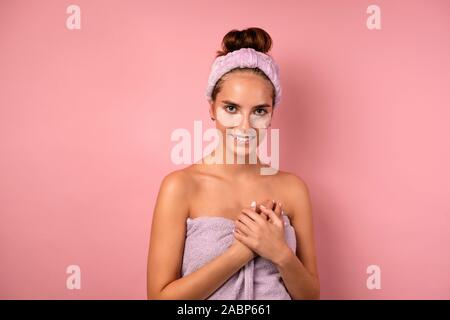 Ein Mädchen mit einem Verband am Kopf und Patches unter ihren Augen steht auf einem rosa Hintergrund und ihre Hände auf der Brust. Stockfoto