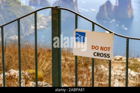 ANACAPRI, ITALIEN - AUGUST 2019: Warnschild an einem Metallzaun oberhalb einer Klippe mit Blick auf das Meer in Anacapri auf der Insel Capri. Stockfoto