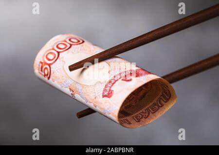 Chinese sticks halten fünf Tausend Rubel, close-up. Internationale Beziehungen zwischen Russland und China Stockfoto