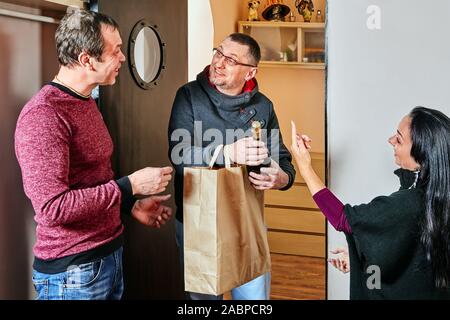 Mann und Frau sind ein Geschenk für Ihren Freund. Kam ein Mann, seine Freunde zu besuchen und sie gaben ihm ein Geschenk und eine Flasche Champagner für die Geburt Stockfoto