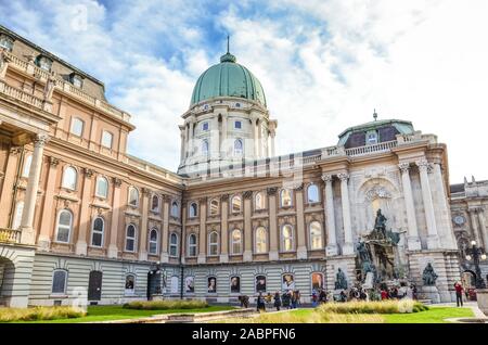 Budapest, Ungarn - Nov 6, 2019: Buda Castle mit monumentalen Brunnen Gruppe als Matthias Brunnen im Hof bekannt. Fassade mit Säulen, arch Windows und Kuppel. Touristen auf den Platz. Stockfoto