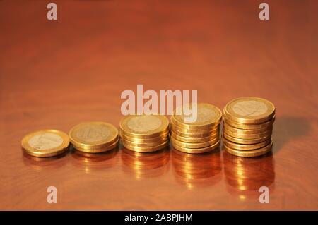 Ein paar Stapel von Euro Münzen gestapelt auf einem natürlichen hölzernen Tisch, wo die Münzen reflektiert werden Stockfoto