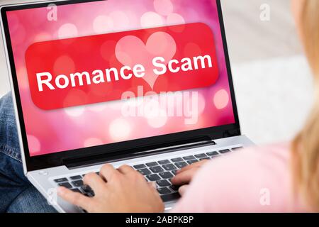 Nahaufnahme einer Frau mit Laptop mit Romantik Scam Anwendung auf dem Bildschirm Zu Hause sitzen Stockfoto
