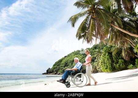 Elder Großvater im Rollstuhl mit Enkelin zu Fuß am Strand. Stockfoto