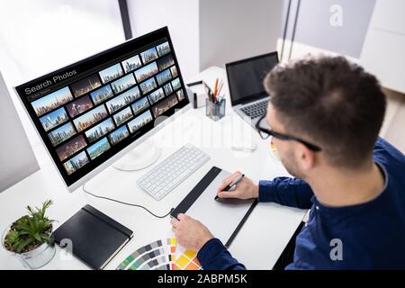 Junge männliche Editor Suche Fotos auf dem Computer im Büro Stockfoto
