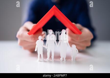 Nahaufnahme der Geschäftsmann Hand Dach über dem Roten Familie stehend auf reflektierende Schreibtisch Stockfoto