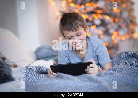 Kind lacht fröhlich, während Sie tablet Bildschirm. Junge das online Spiel gewann. Kind von Gadgets im Urlaub vor Weihnachten. Stockfoto