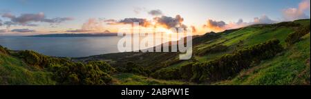 Panoramablick auf die Azoren Sonnenuntergang über das hügelige Landschaft São Jorge mit Pico Insel über das Meer im Hintergrund mit dem Berg von Pico Gipfel. Stockfoto