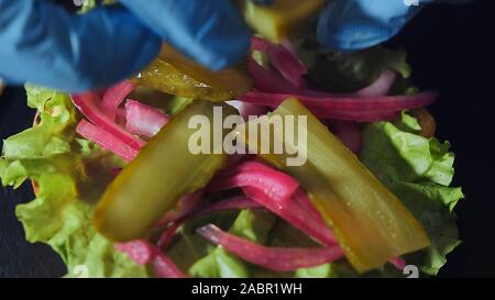 Extra Nahaufnahme eines Chefkoch bereitet einen Hamburger. Hände Köche in Handschuhe anziehen Pickles auf einen Hamburger Stockfoto