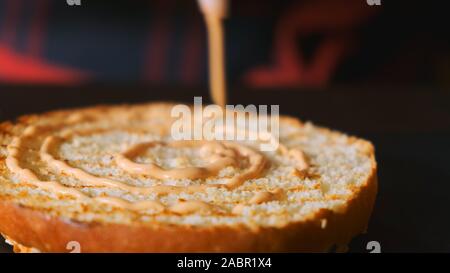 Koch Montage einen Burger. Close-up Cook gießt Soße auf einen Hamburger Bun Stockfoto